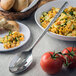 A slotted spoon in a bowl of corn salad with tomatoes.