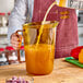 A person pouring orange juice into a Cambro plastic measuring cup.