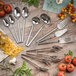 A Carlisle Terra stainless steel serving spoon on a wood surface with other silverware.