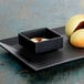 A black square Front of the House porcelain bowl with white sauce on a plate of food.