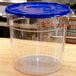 A Carlisle clear plastic food storage container with a blue lid on a wooden counter.