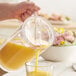 A person using a Carlisle Elan pitcher lid to pour orange juice into a glass.