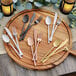A wooden cutting board with Acopa Phoenix stainless steel dinner knives and candles on a table.