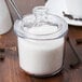 A glass Cambro condiment jar with a slotted lid full of sugar with a spoon.