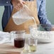 A person using a Choice purple plastic measuring cup to pour milk into a bowl of flour.