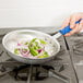 A hand holding a Vollrath Wear-Ever fry pan with onions and peppers cooking.