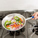 A hand holding a Vollrath Wear-Ever fry pan of vegetables on a stove.