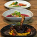 A table with three Front of the House Tides oval porcelain coupe plates of food on it.