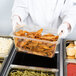 A person in a white uniform holding a Cambro amber plastic food pan filled with food.