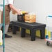 A man in an apron carrying a wooden crate on a black Regency plastic dunnage rack.