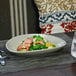 A Tides oval porcelain coupe plate with food on a table.