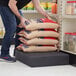 A man using a black plastic Regency end cap to stack bags of flour on a table in a grocery store aisle.