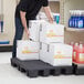 A man using a black plastic Regency display base to stack boxes of soda in a grocery store aisle.