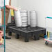 A man holding metal kegs on a black plastic Regency dunnage rack with a slotted top.