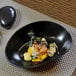 A black oval porcelain bowl filled with food.