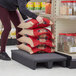 A woman in a black shirt and purple pants putting a stack of bags on a black plastic display base.
