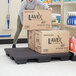 A woman using a Regency black plastic soda case stacker on a counter in a grocery store aisle.