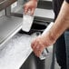 A man pouring ice into a glass from a Regency underbar ice bin with a sliding lid.