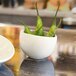 A white Front of the House Tides porcelain bowl filled with green peppers on a table.