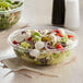 A salad in a Dart clear plastic bowl with a knife.