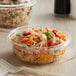 A clear Dart plastic bowl filled with food on a table.