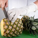 A person wearing a San Jamar D-Shield cut-resistant glove cutting a pineapple.