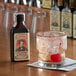 A glass with ice and a cherry next to a bottle of King Floyd's Cherry Cacao Bitters.