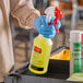 A person in blue gloves using a yellow Rubbermaid spray bottle.