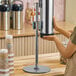 A woman using a silver Modular Countertop Cup Dispenser on a counter.
