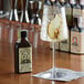 A glass of liquid with a slice of pear in it next to a bottle of King Floyd's Scorched Pear & Ginger Bitters.