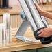 A person using a Modular Countertop Stainless Steel Cup Dispenser on a counter.