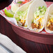 An oval raspberry polypropylene deli server with tacos, limes, and a fork.