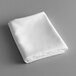 A folded white rectangular Intedge table cloth on a gray surface.