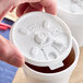 A hand using a Dart white plastic lid on a cup of brown liquid.