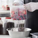 A gloved hand uses a Cambro 1/6 size colander to rinse strawberries in a plastic container.