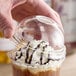 A hand holding a Dart clear plastic dome lid over a drink with whipped cream.