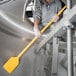 A person using a yellow Carlisle Sparta paddle with a yellow pole to clean a metal pipe.