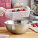 A person using a Cambro translucent plastic container as a colander to rinse strawberries.