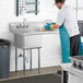 A man in a white shirt and blue apron washing dishes in a Steelton commercial sink with a right drainboard.