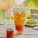 An Arcoroc white plastic pitcher of iced tea on an outdoor table next to a plate of salad.