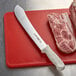 A Dexter-Russell Sani-Safe butcher knife on a cutting board next to meat.