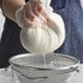 A person in gloves holding a white ball of cheese in San Jamar cheesecloth.