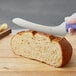 A person cutting a loaf of bread with a Dexter-Russell purple scalloped bread knife.