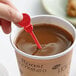 A hand holding a Royal Paper red beverage stirrer in a cup of coffee.