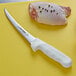 A Dexter-Russell narrow curved boning knife next to a raw chicken breast on a cutting board.