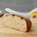 A person using a Dexter-Russell yellow scalloped bread knife to cut a loaf of bread.