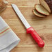 A Dexter-Russell bread knife with a red handle next to slices of bread.