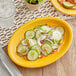 An Acopa mango orange stoneware oval platter with cucumber salad on it.