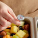 A person's hand using a Taylor pocket probe thermometer to check the temperature of fruit salad.