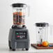 A Waring commercial food blender with fruit in it on a counter.